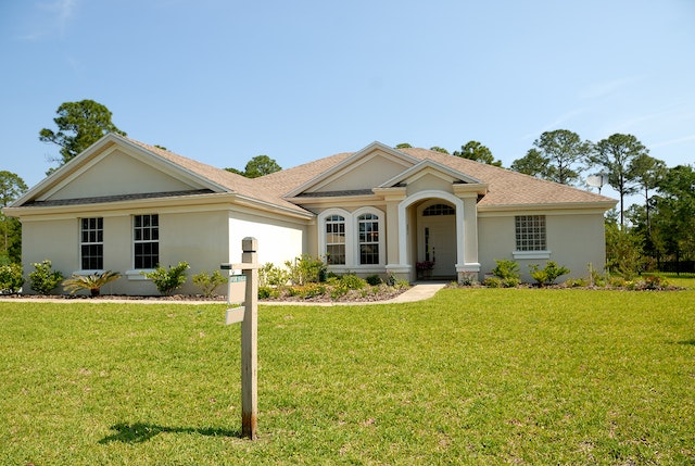 a beige house with a for sale sign on the lawn